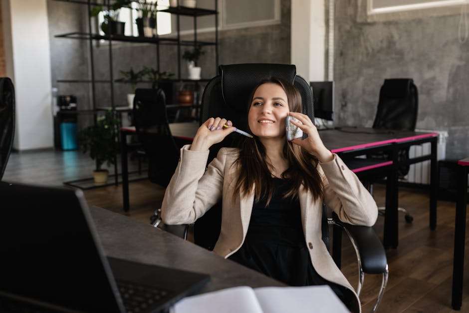 Image of a smiling receptionist at a desk, speaking on the phone with a welcoming aura, set in a modern office environment.