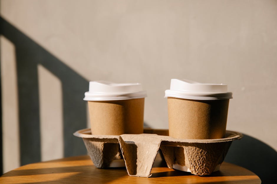 A steaming cup of specialty coffee surrounded by coffee beans and eco-friendly packaging to highlight sustainability
