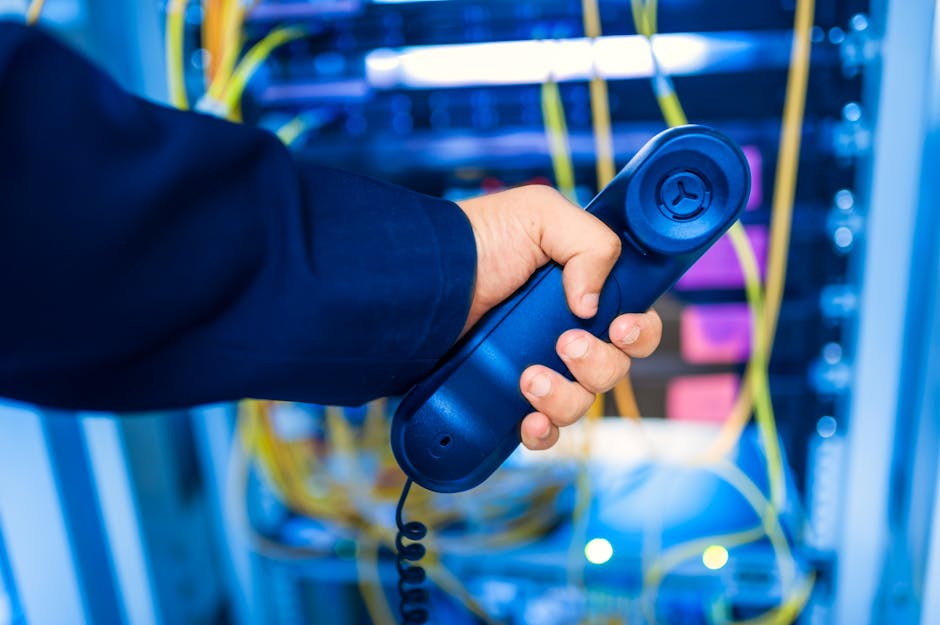 A business professional troubleshooting a VoIP phone system while interacting with Google Voice on a laptop