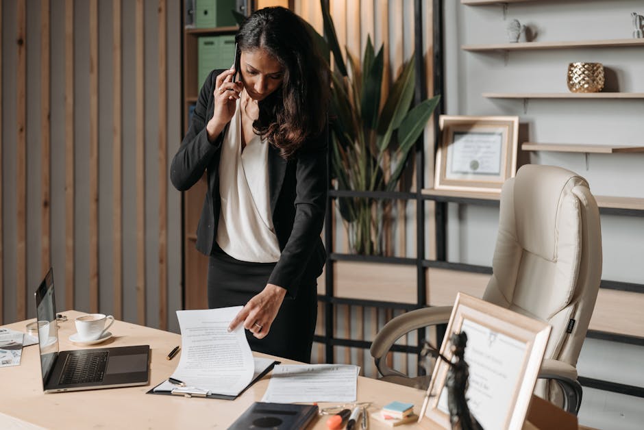 A business professional on a call, reflecting on legalities, with papers and a laptop in front.